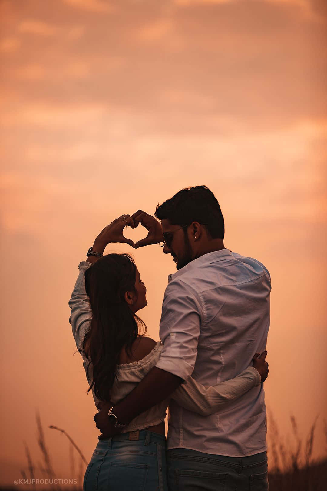 দম্পতি সূর্যাস্তের সময় ঘাসের মাঠে হাত দিয়ে হৃদয় তৈরি করছে ওয়ালপেপার